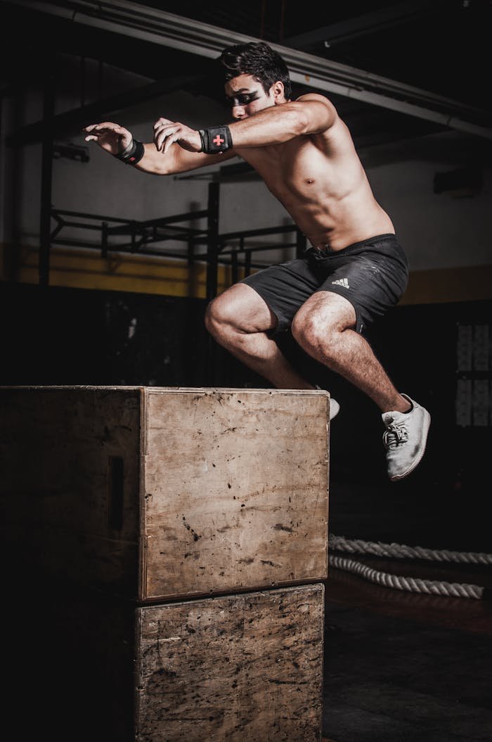 our-services-1 Shirtless man showcasing strength and fitness with a box jump in an indoor gym setting.