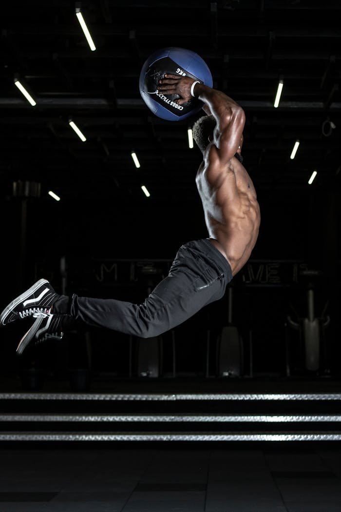 contact-img Muscular athlete performing a high jump with a medicine ball in a gym, showcasing strength and fitness.